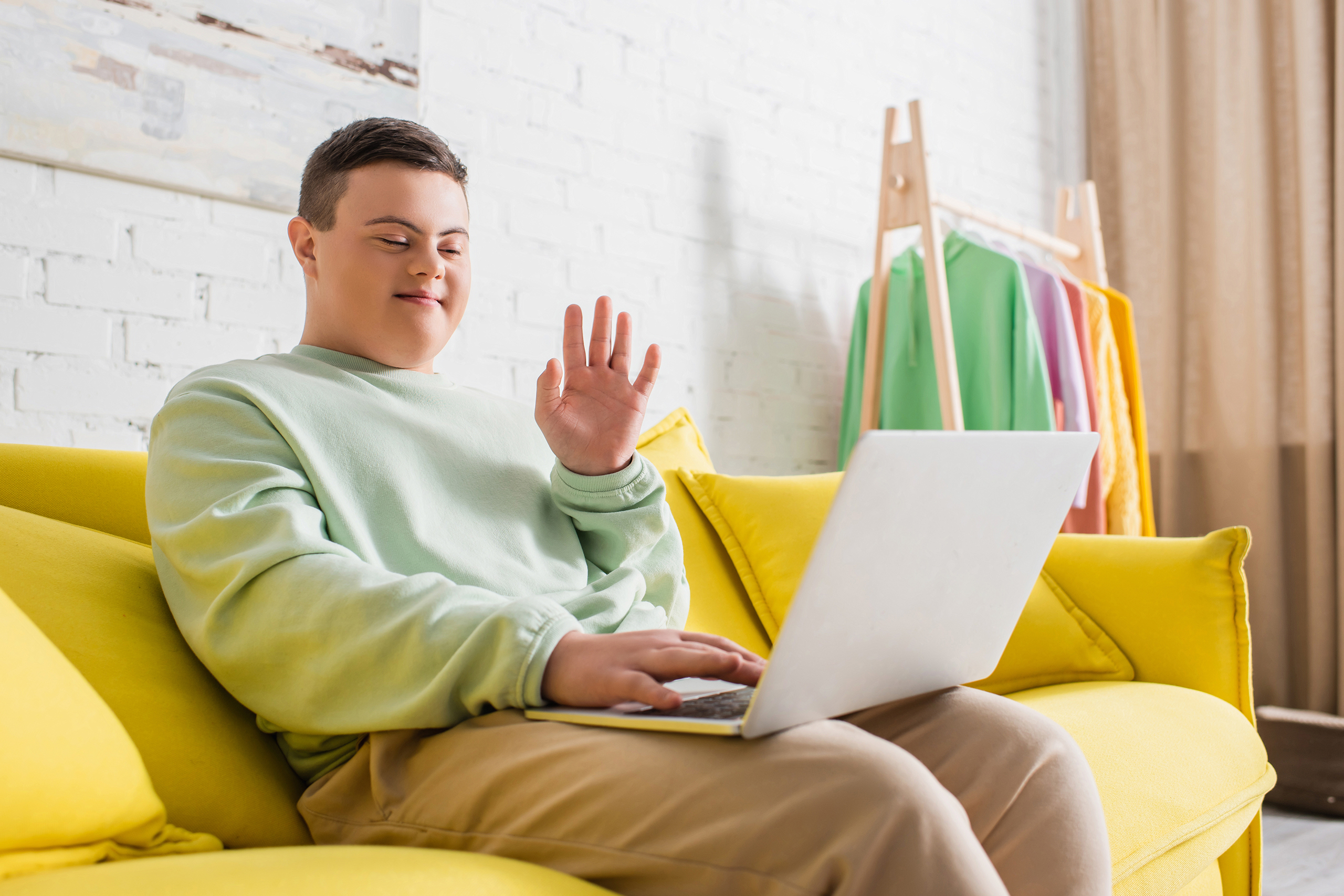 Teenager with down syndrome having video call on laptop on couch at home,stock image